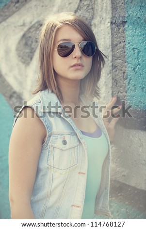 Teen girl in sunglasses near graffiti wall.
