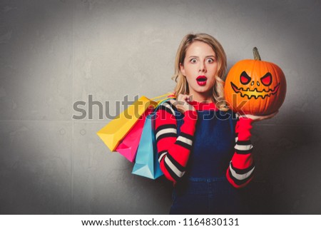 Young style girl in jeans clothes with shopping bags and halloween pumpkin on grey background.