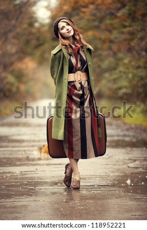 Style redhead girl with suitcase at beautiful autumn alley.