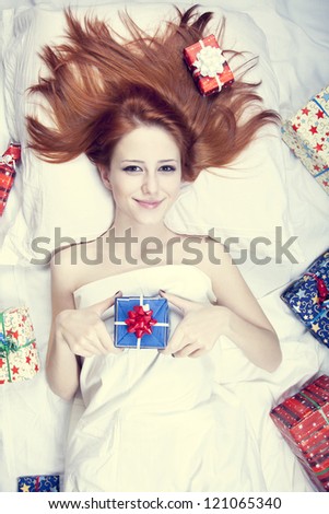 Redhead girl in bed with gifts. Photo in warm tone style.