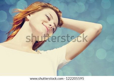 Portrait of redhead girl in white on blue sky with bokeh at background.