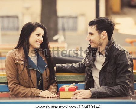 The young man gives a gift to a young girl in the cafe and they are kissing.