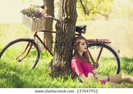 Beautiful girl sitting near bike and tree at rest in forest. Photo in retro style.