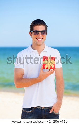 Handsome young man with gift at beach background