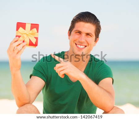Handsome young man with gift at beach background