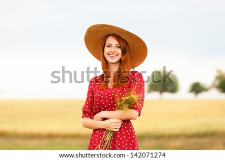 Redhead girl in red dress at wheat field
