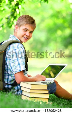 Teen boy with books and laptop in the park.