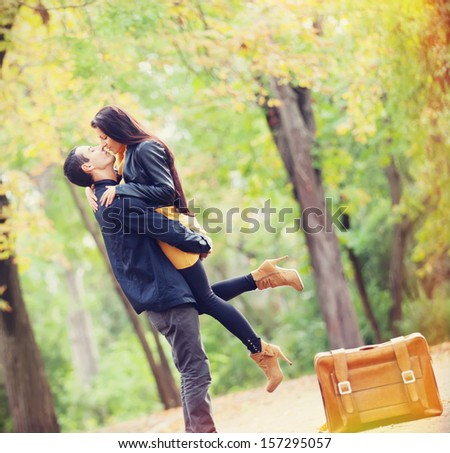 Couple with suitcase kissing at alley in the park