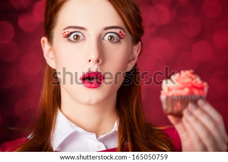Redhead girl with cake. Photo red background with bokeh.