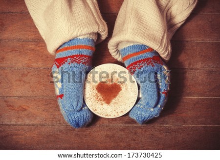 Hands in mittens holding hot cup of coffee. Photo with focus on heart.
