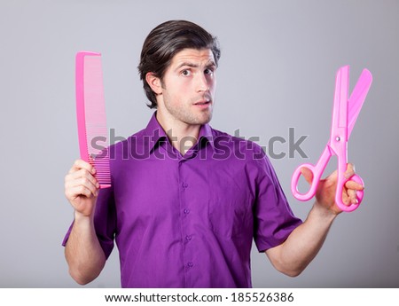 Man with huge scissors and comb on gray background.