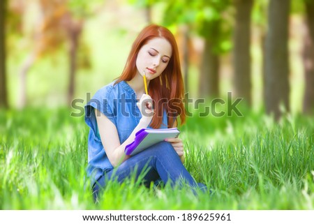 Portrait of young redhead smiling woman with notebook in the city park.