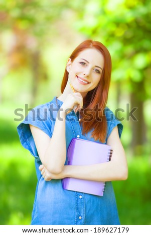 Portrait of young redhead smiling woman with notebook in the city park.