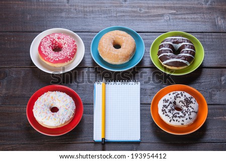 Notebook, donuts and pencil on wooden table.
