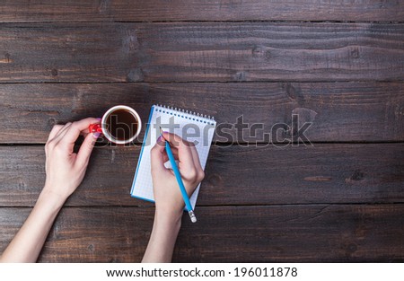 Hands holding notebook and coffee cup.