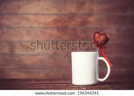 Cup of coffee with heart shape toy on wooden table.