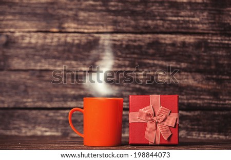 Gift box and cup of coffee on wooden table.