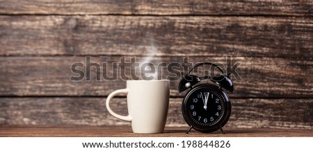 Tea or coffee cup and alarm clock on wooden table.