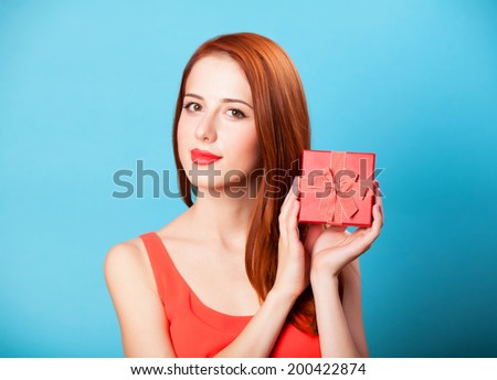 Smiling redhead women with gift on blue background.