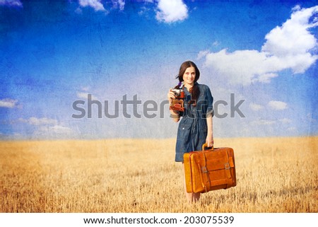 Brunette girl with suitcase on countryside. Photo in old color image style.