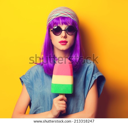 Beautiful girl with violet hair in sunglasses and ice-cream on yellow background.