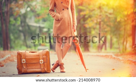 Girl in coat with umbrella and suitcase in the park.