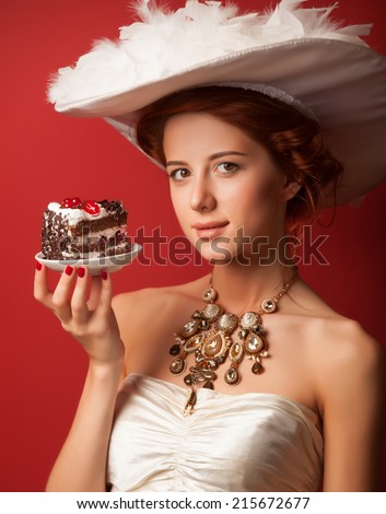 Portrait of redhead edwardian women with cake on red background.