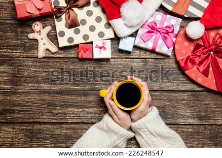 Female holding cup of coffee on wooden table near christmas gifts