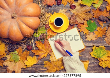 Female hand writing something in notebook on autumn background.