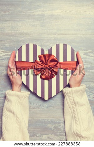 Female hands holding gift on wooden table.