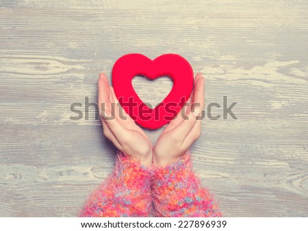 Female holding heart shape toy on a wooden background.