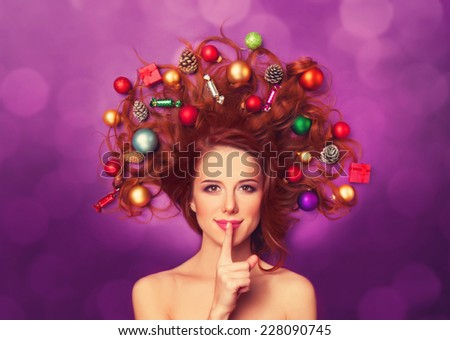 Beautiful redhead girl with christmas toys and canes in hair on violet background