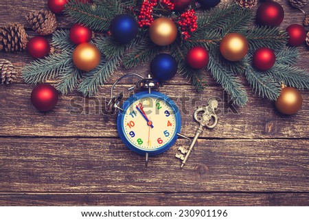 Alarm clock and vintage key near Pine branches on wooden table.