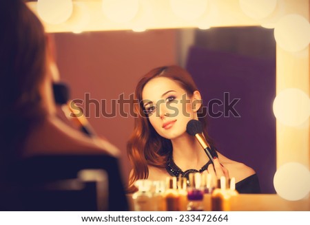 Beautiful redhead women applying makeup near mirror