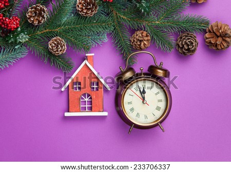 Alarm clock and toy house with pine branch on violet background.