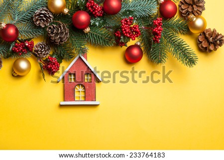 Toy house and pine branches with toys on yellow background.