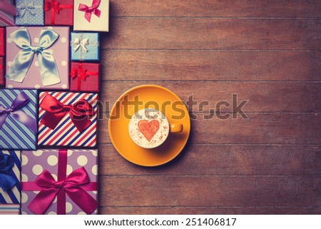 Cup of Cappuccino with heart shape symbol and gift boxes on wooden background