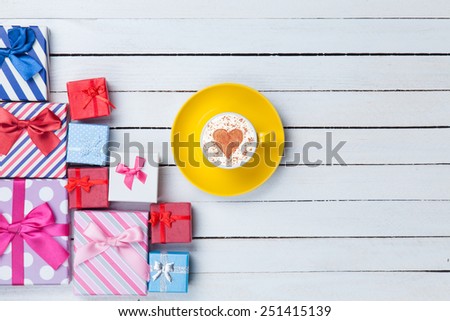 Cup of Cappuccino with heart shape symbol and gift boxes on white wooden background