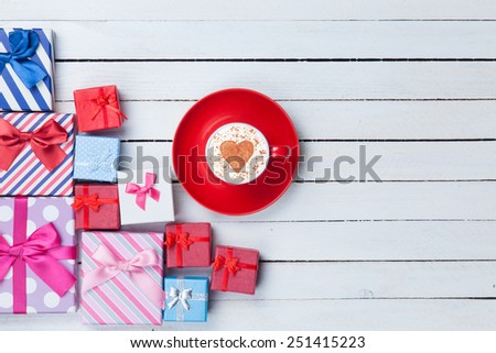 Cup of Cappuccino with heart shape symbol and gift boxes on white wooden background
