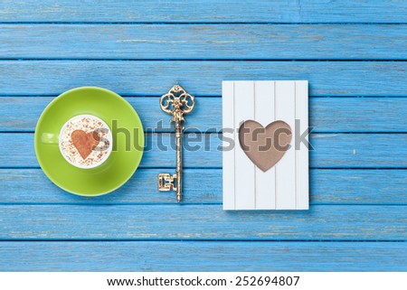 Cup of Cappuccino with heart shape symbol, key and photo frame on blue wooden background.