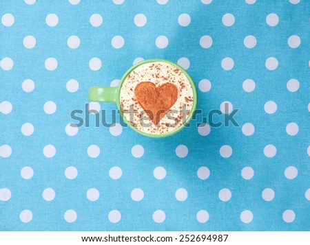 Cup of Cappuccino with heart shape symbol on polka dot background.