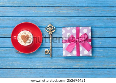Cup of Cappuccino with heart shape symbol, key and gift box blue wooden background.