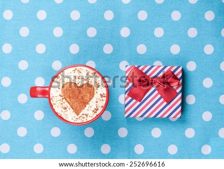 Cup of Cappuccino with heart shape symbol and gift box on polka dot background.