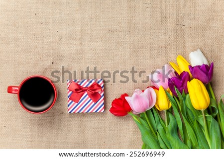 Cup of coffee and gift with flowers on jute background