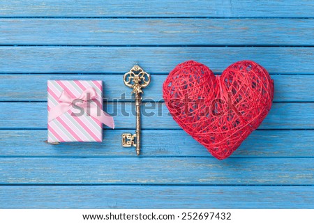 Heart shape toy with key and gift box on blue wooden background.
