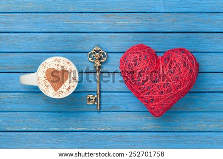 Cup of Cappuccino with heart shape symbol, key and toy on blue wooden background.