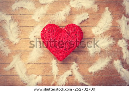Toy heart shape and feathers on wooden background.
