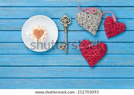 Cup of Cappuccino with heart shape symbol, key and toys on blue wooden background.