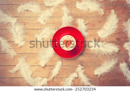 Cup of Cappuccino with heart shape symbol and feathers on wooden background