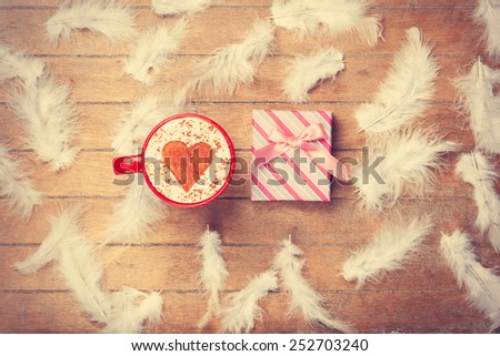 Cup of Cappuccino with heart shape symbol and feathers with gift on wooden background